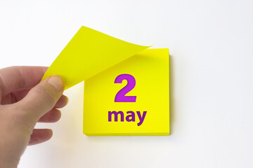 May 2nd. Day 2 of month, Calendar date. Hand rips off the yellow sheet of the calendar. Spring month, day of the year concept.