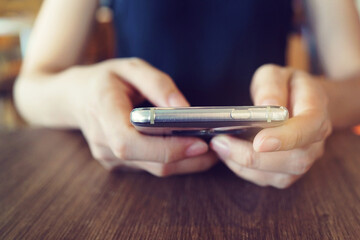 Woman hand holding smart phone in a coffee house, hipster girl using mobile phone during coffee break.