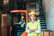 © BigBlues - Portrait of asian woman. warehouse Smiling worker standing with arms crossed in large warehouse with goods. in background driver at Warehouse forklift loader works with goods.