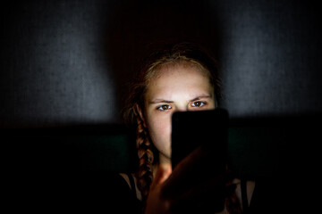 portrait of young teenager redhead girl with long hair with smartphone in dark room