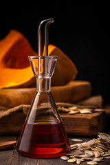 Fresh organic pumpkin seed`s oil in the glass bottle on rustic wooden background close up selective focus