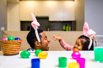 Wall Mural - happy mixed race family celebrating Easter, painting eggs with brush smiling and laughing