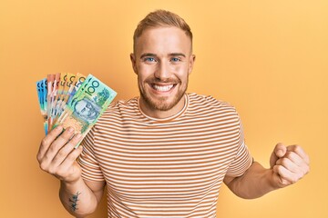 Wall Mural - Young caucasian man holding australian dollars screaming proud, celebrating victory and success very excited with raised arm