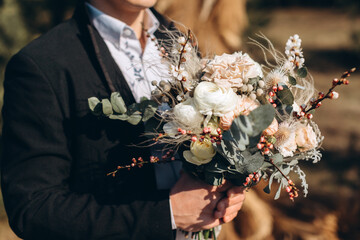 Wall Mural - the bride’s bouquet in the hands of the groom, a black suit of the groom, a wedding bouquet of the bride with peonies