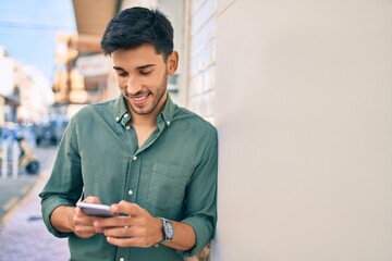 young latin man smiling happy using smartphone at the city.