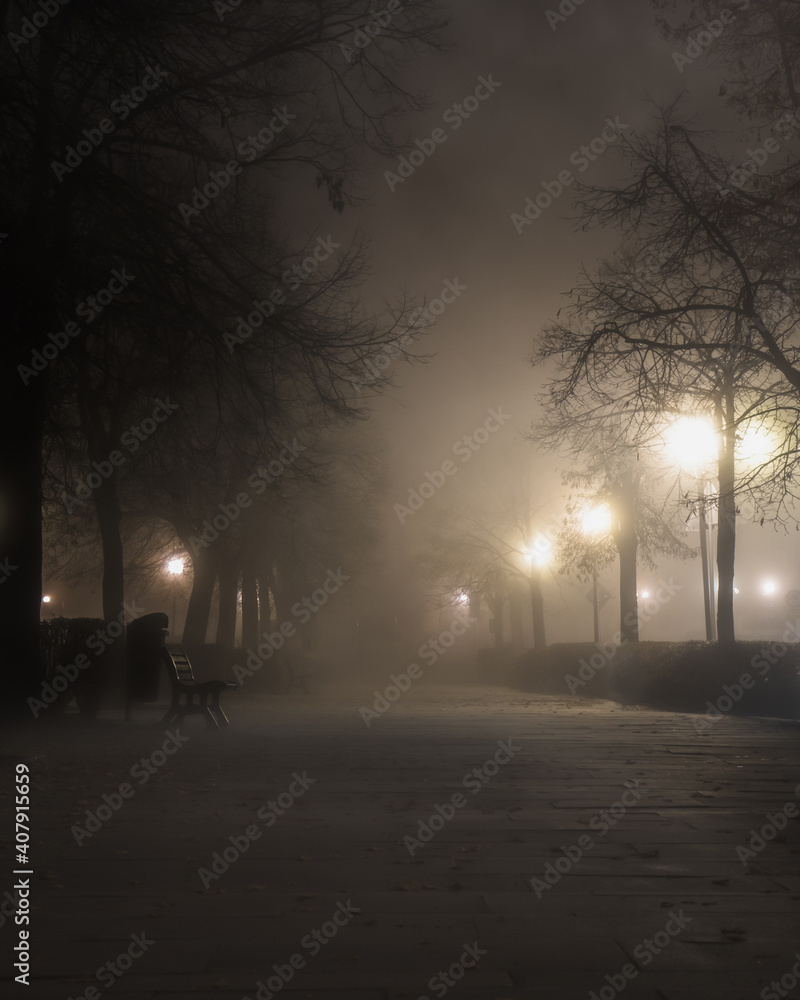 Street in city shrouded in fog and lighted by street lights. In the ...