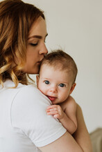 Beautiful Mom Hugs And Kisses The Newborn In The Studio On A White Background. A Young Mother In A White Bodysuit Hugs And Kisses Her Newborn Daughter In The Studio.