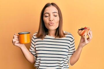 Canvas Print - Young beautiful woman drinking coffee and eating pastry looking at the camera blowing a kiss being lovely and sexy. love expression.