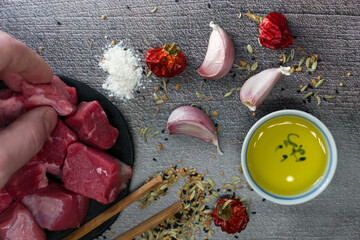 Sticker - Top view of a male hand taking raw cut meat from a table with garlic cloves, dried pepper, oil