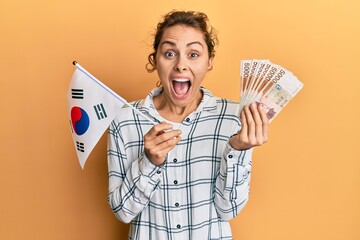 Poster - Young brunette woman holding south korean won banknotes celebrating crazy and amazed for success with open eyes screaming excited.