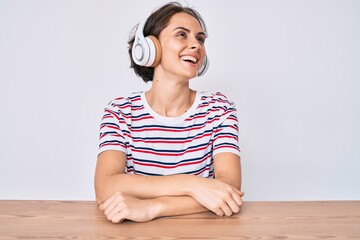 Sticker - Young hispanic woman using headphones sitting on the table looking away to side with smile on face, natural expression. laughing confident.