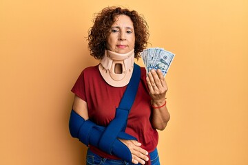 Poster - Beautiful middle age mature woman wearing cervical collar and sling holding insurance dollars relaxed with serious expression on face. simple and natural looking at the camera.