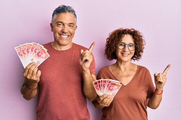 Poster - Beautiful middle age couple holding 20 israel shekels banknotes smiling happy pointing with hand and finger to the side