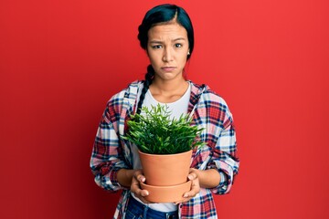 Sticker - Beautiful hispanic woman wearing gardener shirt holding plant pot skeptic and nervous, frowning upset because of problem. negative person.