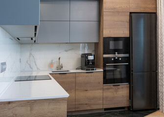 The interior of the studio kitchen is decorated in gray tones with wooden spies. Kitchen appliances and top cabinets are black. The table top is white. Backsplash from marble.