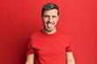 Handsome caucasian man wearing casual red tshirt sticking tongue out happy with funny expression. emotion concept.