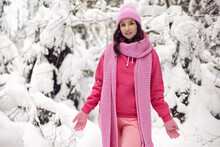 Woman In Pink Clothes A Jacket A Knitted Scarf And A Hat Stands In A Snowy Forest In Winter