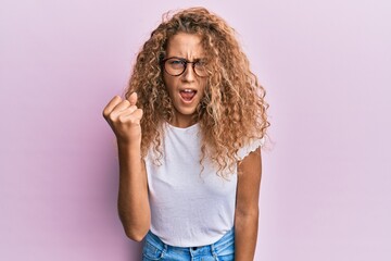 Wall Mural - Beautiful caucasian teenager girl wearing white t-shirt over pink background angry and mad raising fist frustrated and furious while shouting with anger. rage and aggressive concept.