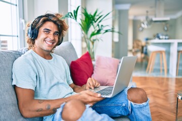 Wall Mural - Young hispanic man smiling happy using laptop and headphones at home