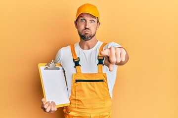 Sticker - Young handsome man wearing courier uniform holding clipboard puffing cheeks with funny face. mouth inflated with air, catching air.