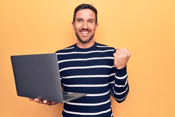 Wall Mural - Young handsome man working using laptop standing over isolated yellow background screaming proud, celebrating victory and success very excited with raised arm