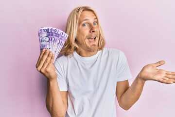 Sticker - Caucasian young man with long hair holding 100 philippine peso banknotes celebrating achievement with happy smile and winner expression with raised hand