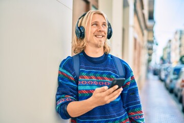 Young scandinavian student man smiling happy using smartphone and headphones at the city.