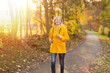 canvas print picture - Weißhaarige Grauhaarige Frau spaziert im Park Herbst Sonnenstrahlen gelbe Regenmantel 