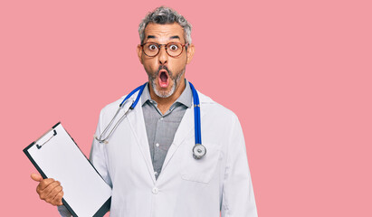 Sticker - Middle age grey-haired man wearing doctor stethoscope holding clipboard scared and amazed with open mouth for surprise, disbelief face