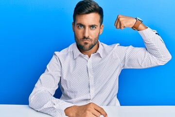 Sticker - Handsome hispanic man wearing business clothes sitting on the table strong person showing arm muscle, confident and proud of power