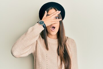 Poster - Young brunette woman wearing french look with beret peeking in shock covering face and eyes with hand, looking through fingers with embarrassed expression.