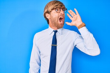 Canvas Print - Young blond man wearing business clothes and glasses shouting and screaming loud to side with hand on mouth. communication concept.