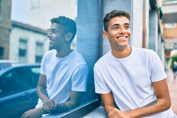 Wall Mural - Young latin man smiling happy leaning on the wall at the city.