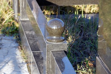 Sticker - part of a black decorative marble barrier with a ball on granite in a cemetery