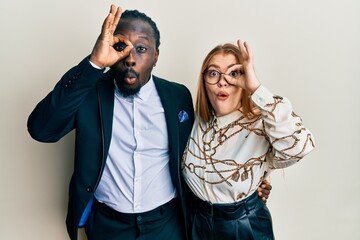 Canvas Print - Young interracial couple wearing business and elegant clothes doing ok gesture shocked with surprised face, eye looking through fingers. unbelieving expression.