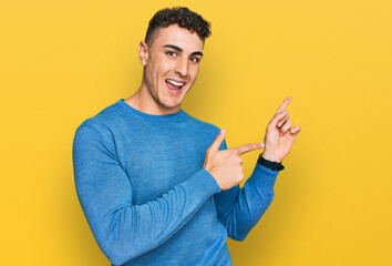 Hispanic young man wearing casual clothes smiling and looking at the camera pointing with two hands and fingers to the side.