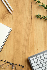 Wall Mural - Feminine workspace top view. Flat lay keyboard, paper notebook, pencils, glasses, eucalyptus leaves on wooden table. Modern home office desk, overhead