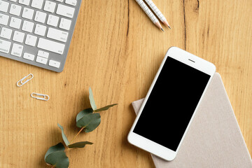 Wall Mural - Modern office desk top view. Flat lay smartphone with empty screen mockup, pc keyboard, eucalyptus leaf, stationery on wooden table