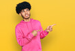 Young african american man with afro hair wearing casual pink sweatshirt pointing aside worried and nervous with both hands, concerned and surprised expression
