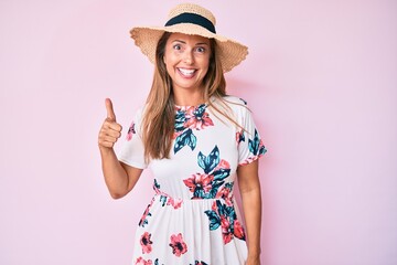 Canvas Print - Middle age hispanic woman wearing summer hat smiling happy and positive, thumb up doing excellent and approval sign