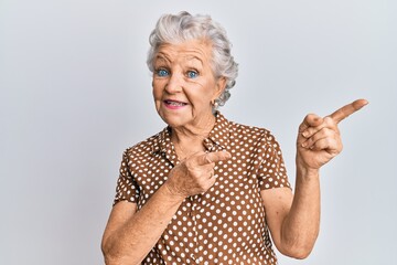 Wall Mural - Senior grey-haired woman wearing casual clothes smiling and looking at the camera pointing with two hands and fingers to the side.