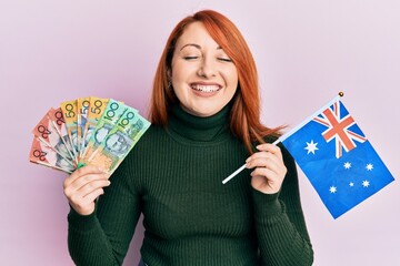 Poster - Beautiful redhead woman holding australian dollars and australia flag smiling and laughing hard out loud because funny crazy joke.