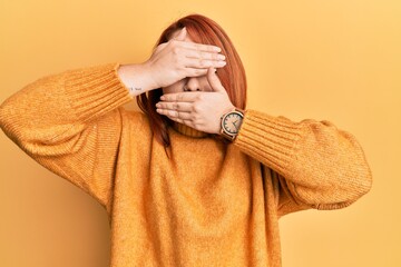 Wall Mural - Beautiful redhead woman wearing casual winter sweater over yellow background covering eyes and mouth with hands, surprised and shocked. hiding emotion