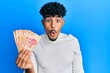 © Krakenimages.com - Young arab handsome man holding 100 mexican pesos banknotes scared and amazed with open mouth for surprise, disbelief face