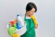 © Krakenimages.com - Young brunette woman with short hair wearing apron holding cleaning products feeling unwell and coughing as symptom for cold or bronchitis. health care concept.