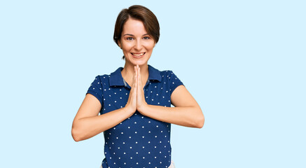 Young brunette woman with short hair wearing casual clothes praying with hands together asking for forgiveness smiling confident.