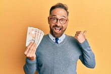 Handsome Middle Age Man Holding 10 United Kingdom Pounds Banknotes Pointing Thumb Up To The Side Smiling Happy With Open Mouth