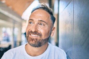 Middle age handsome man smiling happy leaning on the wall at the city.