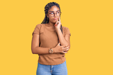 Canvas Print - Young african american woman with braids wearing casual clothes and glasses serious face thinking about question with hand on chin, thoughtful about confusing idea