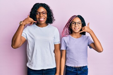 Poster - Beautiful african american mother and daughter wearing casual clothes and glasses smiling doing phone gesture with hand and fingers like talking on the telephone. communicating concepts.